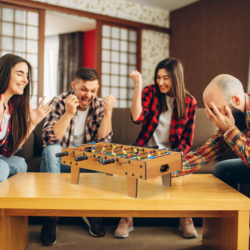 Mehrfarbiger Tischkicker auf einem Tisch mit spielenden Personen im Hintergrund.